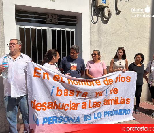La familia, acompañada por vecinos y vecinas del edificio, se concentra frente a su portal tras una pancarta que reza: “En el nombre de Dios, basta ya de desahuciar a las familias. Las personas son lo primero” | Dominic D. Skerrett