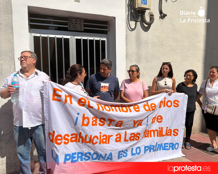 La familia, acompañada por vecinos y vecinas del edificio, se concentra frente a su portal tras una pancarta que reza: “En el nombre de Dios, basta ya de desahuciar a las familias. Las personas son lo primero” | Dominic D. Skerrett